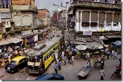 A tram winds its way through the streets of Calcutta. Dirty, hot, smoggy, friendly, that's how one resident describes the city, a place so humid even the bulidings seem to sweat. India, 1996.National Geographic, March 1997, India: Fifty Years of Independence.Magnum Photos, NYC5923, MCS1996002 K010.For McCurry, Calcutta is the most visual city on the planet, spinning with chaos and clutter, crumbling under the weight of its overpopulation, utterly out of control, yet vital and alive.  Vendors spill into streets, which hold a confusion of cars, trams, rickshaws, bicycles and pedestrians.  So how to make this picture?  McCurry looked for an office or apartment on a second floor of a street corner.  'And that is the wonder of the place.  Twenty minutes later, I am on a bed in a couple's apartment, making the picture and staying on for a cup of tea.'-Anthony BannonPhaidon, 55, South Southeast, Iconic Images, final book_iconic   A tram winds its way through the streets of Calcutta.  Dirty, hot, smoggy, friendly, it is a place so humid that even the buildings seem to sweat.      For McCurry, Calcutta is the most visual city on the planet, spinning with chaos and clutter, crumbling under the weight of its overpopulation, utterly out of control, yet vital and alive. Vendors spill into streets, which hold a confusion of cars, trams, rickshaws, bicycles and pedestrians. So how to make this picture? McCurry looked for an office or apartment on a second floor of a street corner. ‘And that is the wonder of the place. Twenty minutes later, I am on a bed in a couple’s apartment, making the picture and staying on for a cup of tea.’